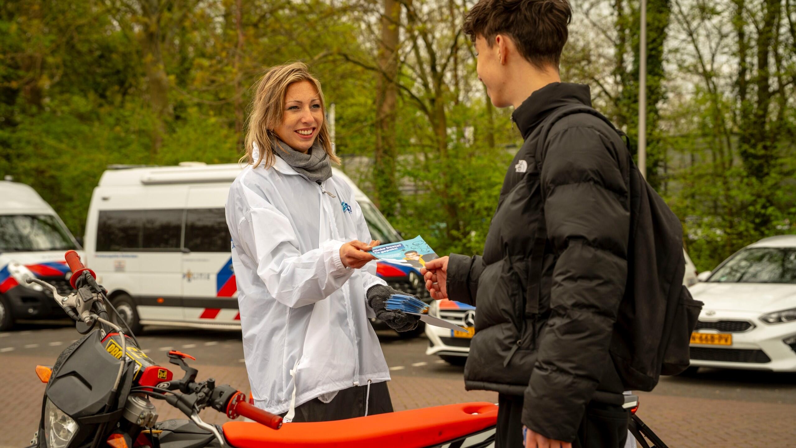 Lid campagneteam overhandigt flyer aan jonge scooterrijder