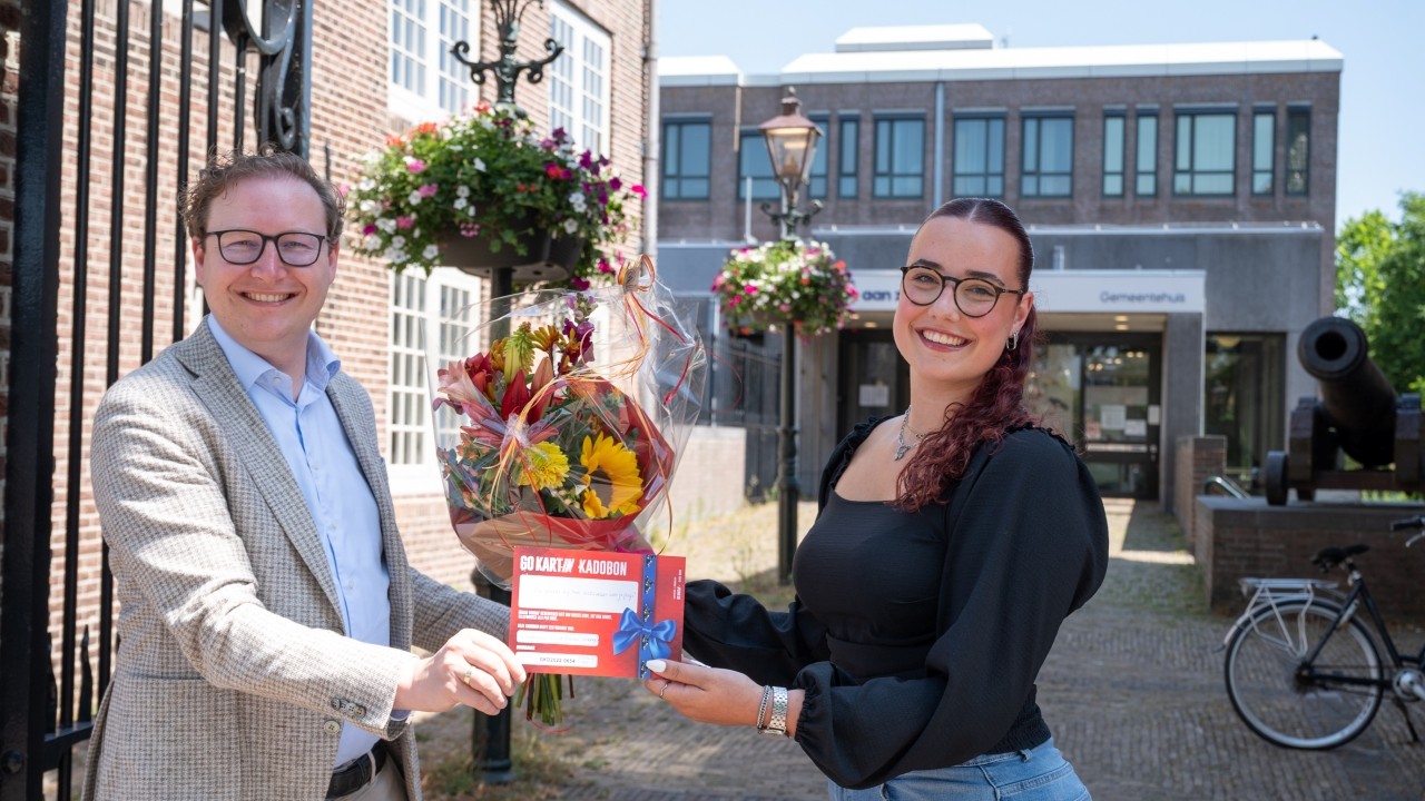 Wethouder overhandigt cadeaucheque en bloemen aan winnares loting