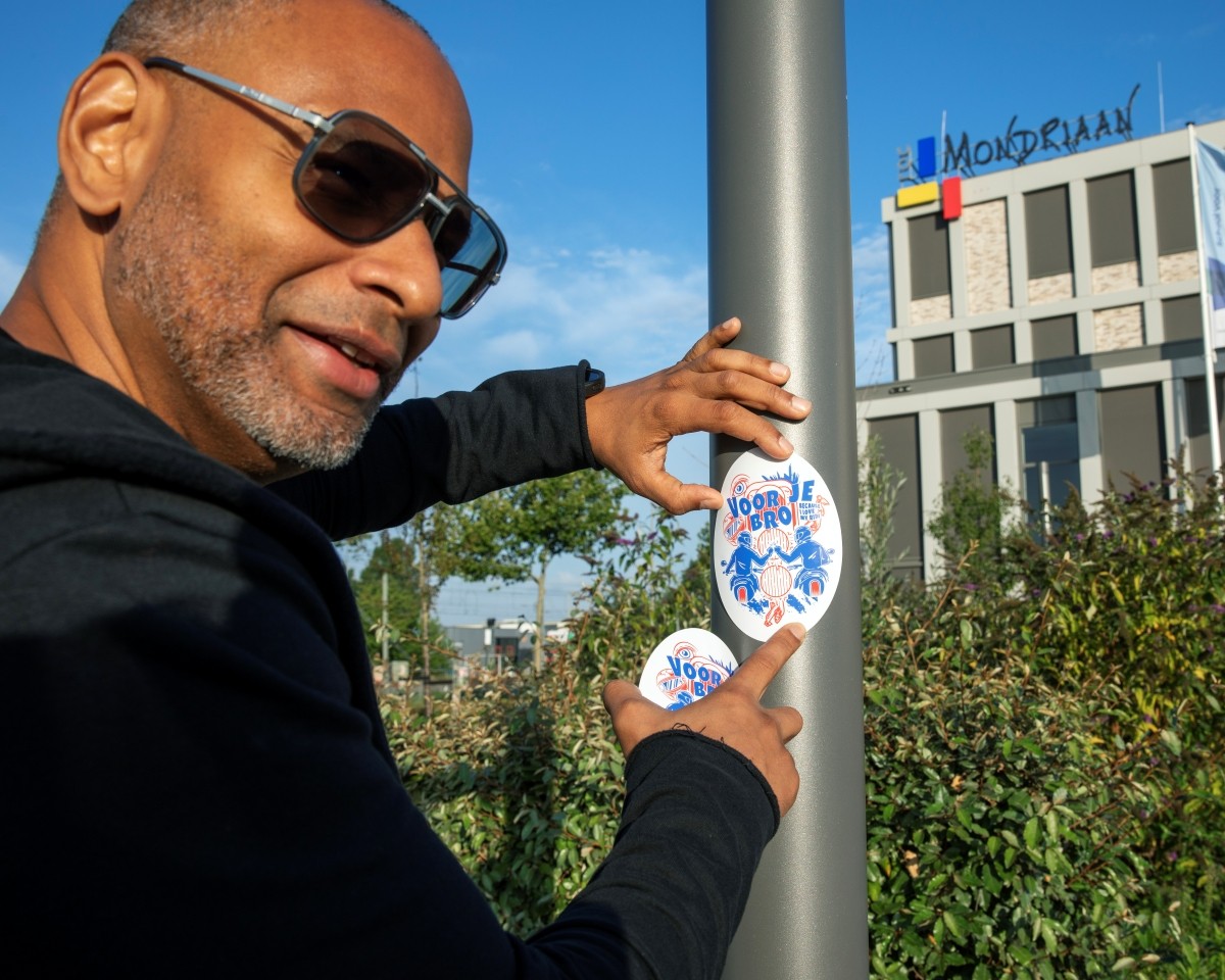Lorenzo Sendar (ROC Mondriaan) plakt sticker jongerencampagne "Voor je Bro" op paal voor de school