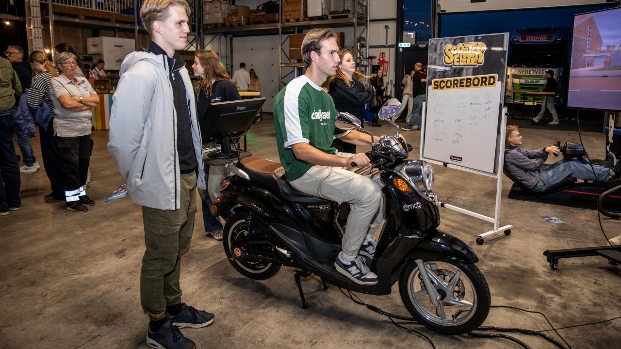 Deelnemer op de scootersimulator, terwijl een andere meekijkt