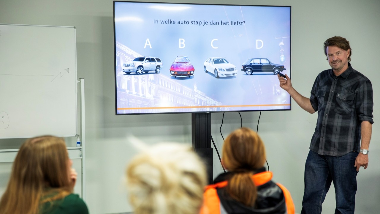 Trainer Henno Oldenbeuving toont vier automodellen en vraagt de deelnemers in welke zij het liefst stappen