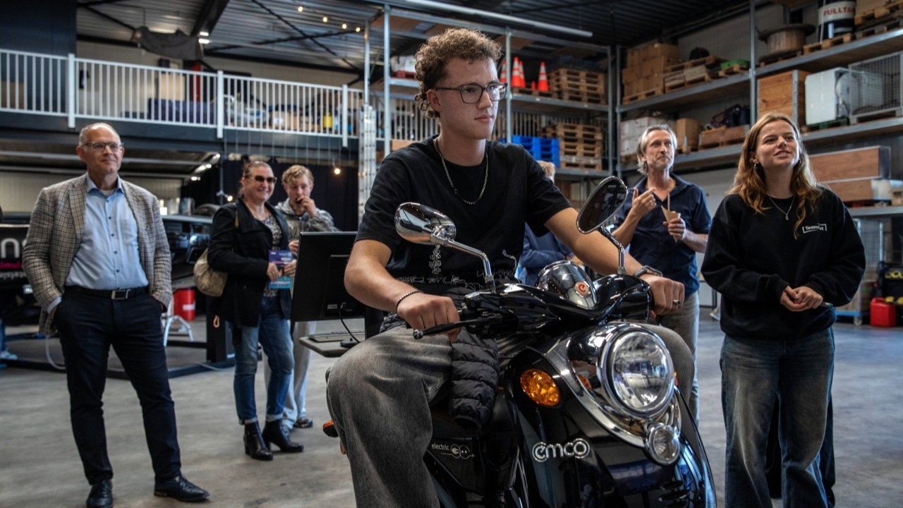 Jongere op de scootersimulator, terwijl anderen op grote schermen meekijken